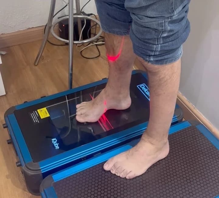 Close do escaneamento 3D: um pé descalço apoiado na plataforma de vidro do scanner, com a linha vermelha do laser passando sobre o pé e a perna durante a leitura